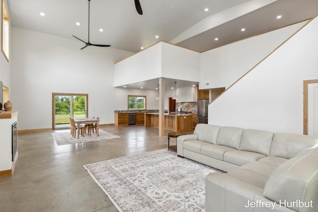 living area with finished concrete flooring, ceiling fan, a towering ceiling, and baseboards