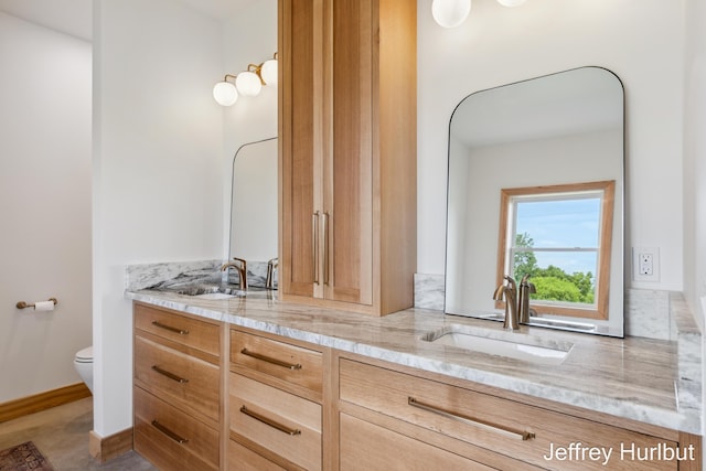 full bathroom with double vanity, a sink, toilet, and baseboards