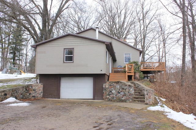 view of snowy exterior with a deck, stairway, an attached garage, and a chimney