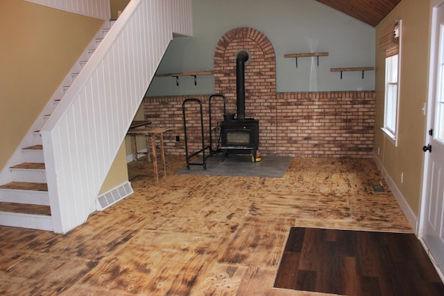 unfurnished living room with lofted ceiling, wood finished floors, visible vents, stairway, and a wood stove