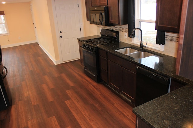 kitchen featuring dark wood-type flooring, a sink, baseboards, dark stone counters, and black appliances