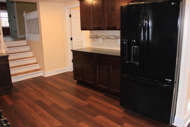 kitchen with dark wood finished floors, black fridge with ice dispenser, backsplash, dark brown cabinetry, and dark stone countertops