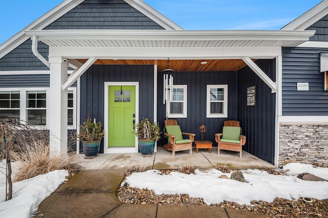 snow covered property entrance with board and batten siding and covered porch