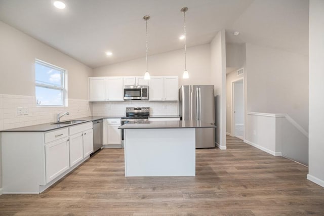 kitchen featuring white cabinetry, appliances with stainless steel finishes, a center island, dark countertops, and decorative light fixtures