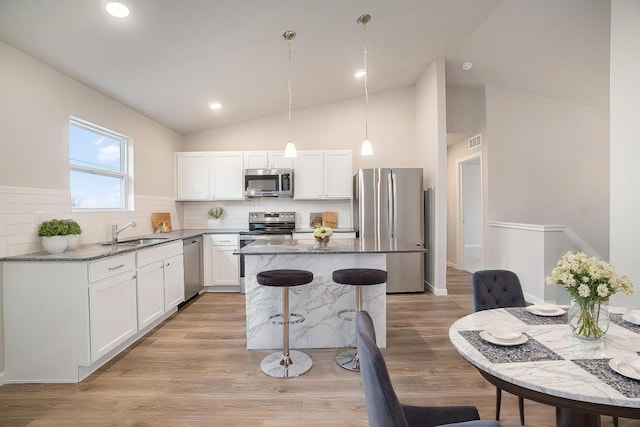 kitchen with stainless steel appliances, a breakfast bar, a sink, white cabinetry, and decorative light fixtures