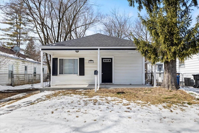 view of front of house featuring covered porch, a shingled roof, and fence