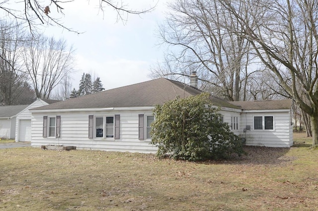 exterior space with a garage, roof with shingles, a chimney, and a yard