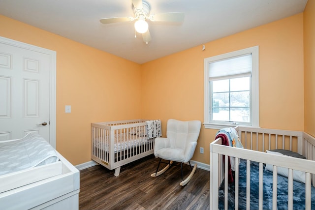 bedroom with dark wood-style floors, ceiling fan, baseboards, and a nursery area