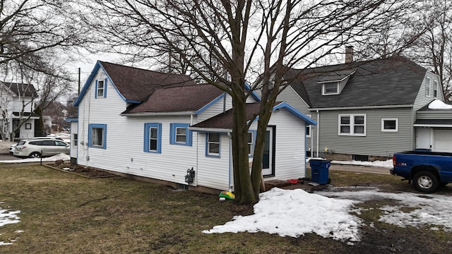 snow covered back of property featuring a yard and a shingled roof