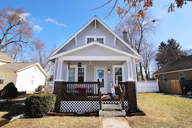 view of front facade featuring covered porch, fence, a chimney, and a front lawn