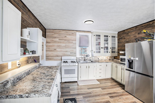 kitchen featuring wood walls, stainless steel refrigerator with ice dispenser, a sink, and white range with gas stovetop