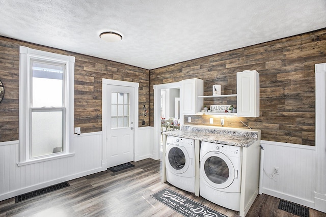 washroom with a wainscoted wall, a textured ceiling, washing machine and dryer, and visible vents