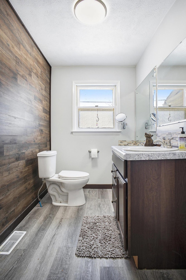 bathroom featuring visible vents, wooden walls, toilet, and wood finished floors