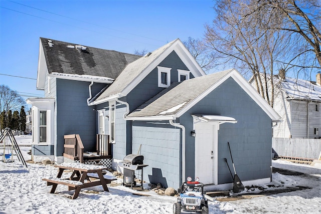 view of snowy exterior featuring a shingled roof, concrete block siding, and fence