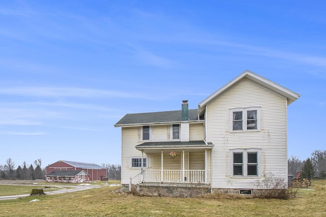 rear view of property with covered porch, a yard, a chimney, and roof with shingles