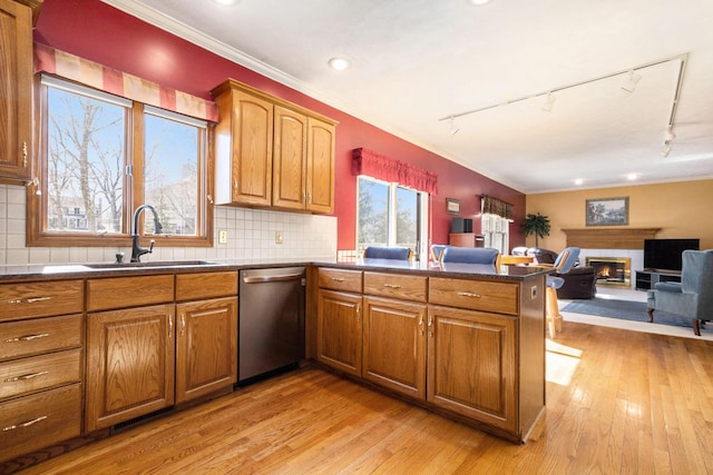 kitchen featuring a peninsula, a sink, dishwasher, dark countertops, and a glass covered fireplace