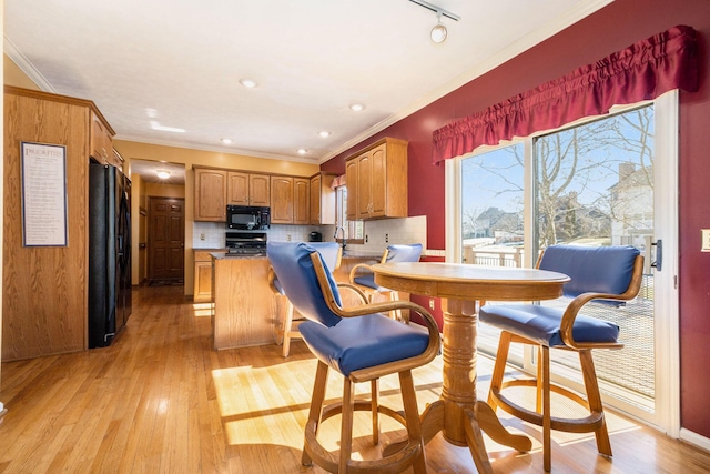 kitchen featuring light wood finished floors, brown cabinets, a peninsula, black appliances, and backsplash