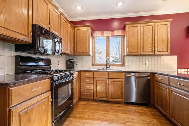 kitchen featuring brown cabinetry, light wood-style flooring, crown molding, black appliances, and a sink