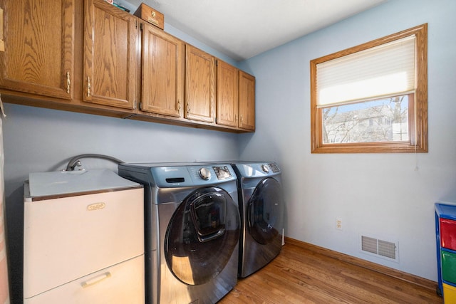 laundry room with visible vents, cabinet space, light wood finished floors, and washing machine and clothes dryer