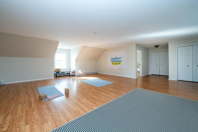 workout room featuring a baseboard radiator, baseboards, vaulted ceiling, and wood finished floors