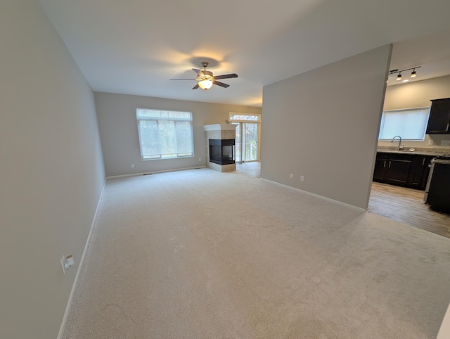 unfurnished living room with light carpet, a fireplace, a sink, a ceiling fan, and baseboards