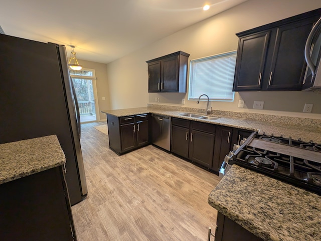 kitchen with stainless steel appliances, a sink, light stone countertops, light wood-type flooring, and a peninsula