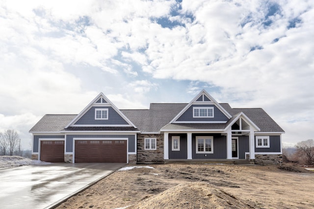 view of front of property featuring a porch, stone siding, roof with shingles, and driveway