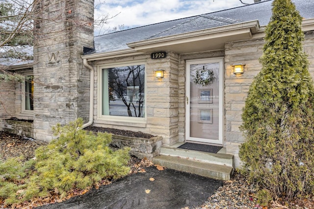 view of exterior entry featuring stone siding, a chimney, and roof with shingles