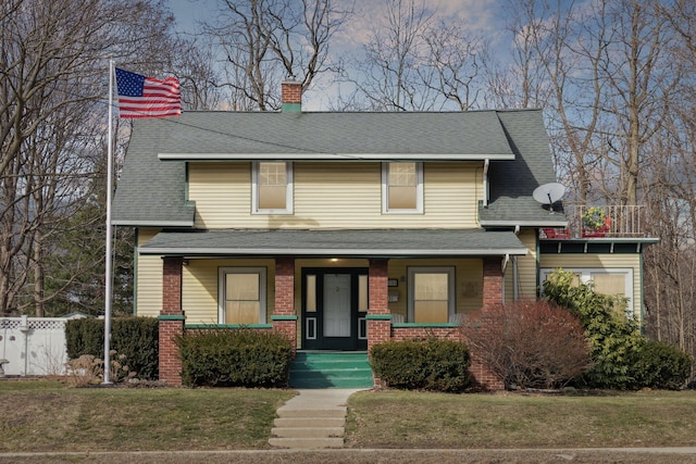 view of front of property featuring brick siding, a chimney, a porch, fence, and a front lawn