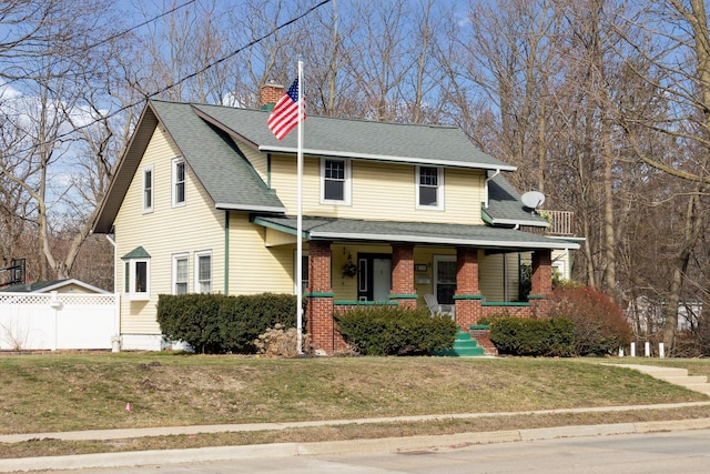 view of front of house featuring brick siding, a chimney, a porch, fence, and a front lawn