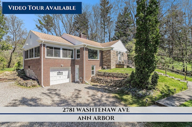 view of front of property featuring a garage, driveway, brick siding, and a chimney