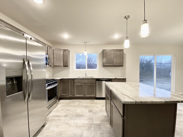 kitchen with light stone counters, a center island, decorative light fixtures, stainless steel appliances, and a sink