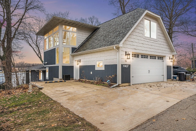 property exterior at dusk with a shingled roof, driveway, and fence