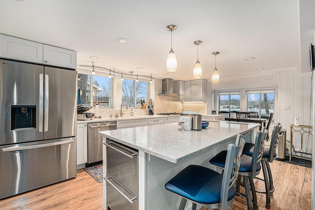 kitchen with light wood-style flooring, appliances with stainless steel finishes, a warming drawer, wall chimney exhaust hood, and a center island