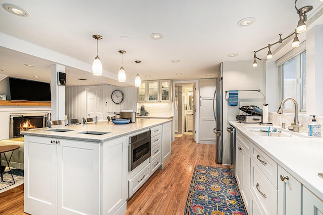 kitchen featuring a sink, stainless steel microwave, tasteful backsplash, white cabinetry, and light wood finished floors