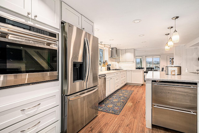 kitchen featuring light wood-type flooring, decorative light fixtures, stainless steel appliances, white cabinets, and light stone countertops