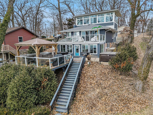 back of property featuring stairway, a balcony, roof with shingles, a hot tub, and a gazebo