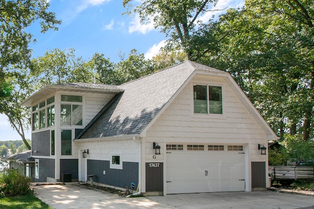 view of side of property featuring concrete driveway, an attached garage, and roof with shingles