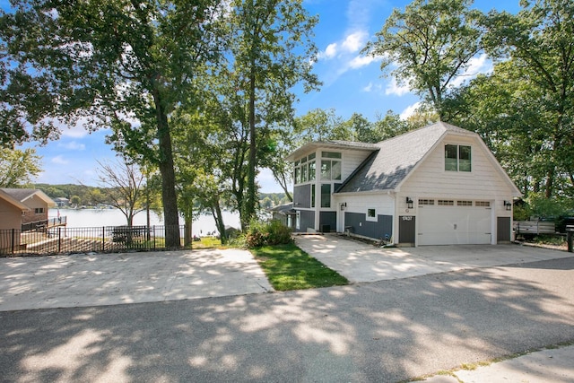 view of front of house with a water view, driveway, fence, an attached garage, and a shingled roof