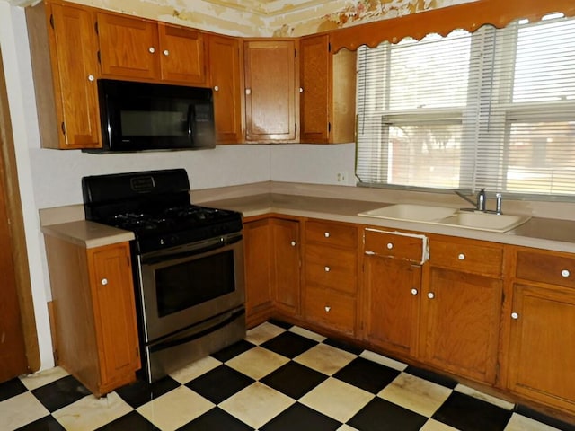 kitchen with black microwave, a sink, stainless steel gas stove, light floors, and brown cabinetry