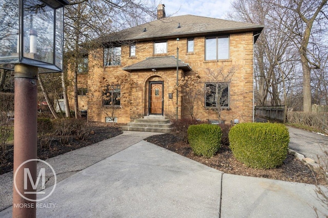 view of front of house featuring brick siding, a chimney, and a shingled roof