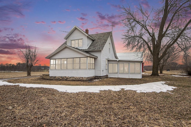 rear view of property featuring a shingled roof, a chimney, and a sunroom