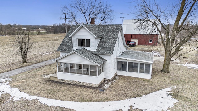 view of front of home with a sunroom, roof with shingles, and a chimney