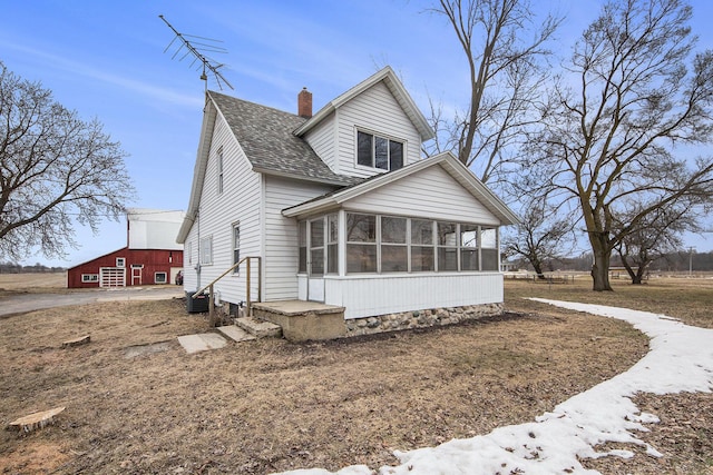 view of front of home with a sunroom, roof with shingles, and a chimney