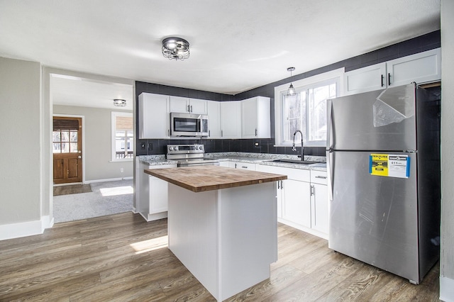 kitchen featuring butcher block countertops, a sink, appliances with stainless steel finishes, and white cabinetry