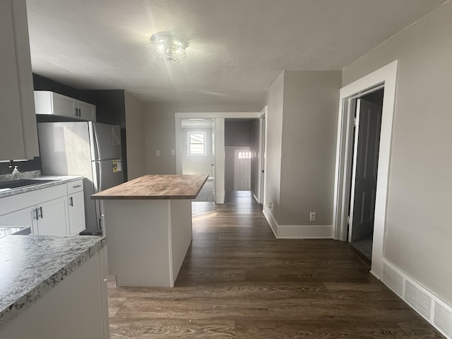 kitchen featuring butcher block counters, dark wood-style flooring, a kitchen island, a sink, and white cabinets