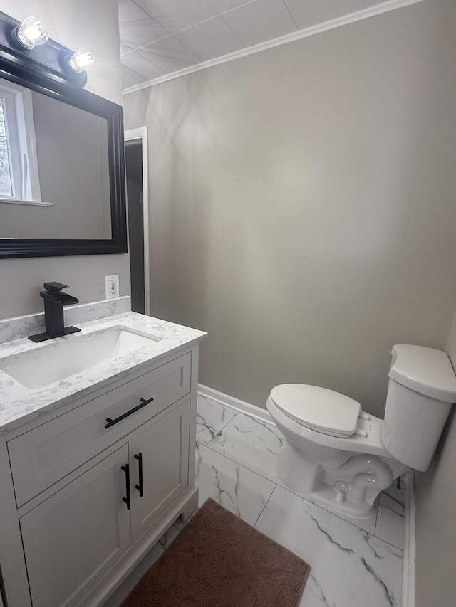 half bath with toilet, vanity, baseboards, marble finish floor, and ornamental molding