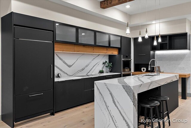 52 E 8th St Ste 210, Holland, MI 49423 - kitchen featuring dark cabinets, double oven, modern cabinets, backsplash, and light stone countertops