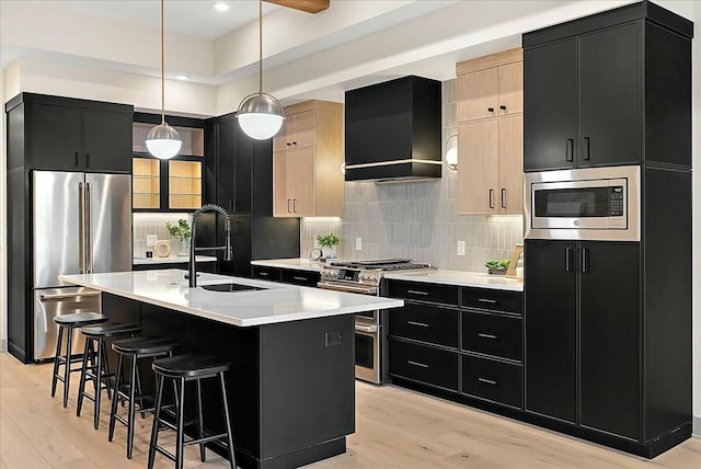 kitchen with a sink, wall chimney exhaust hood, tasteful backsplash, dark cabinetry, and appliances with stainless steel finishes