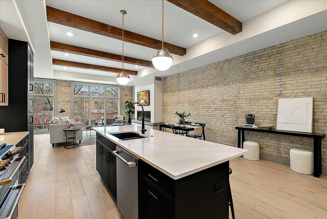 kitchen featuring dishwasher, brick wall, a sink, dark cabinetry, and open floor plan